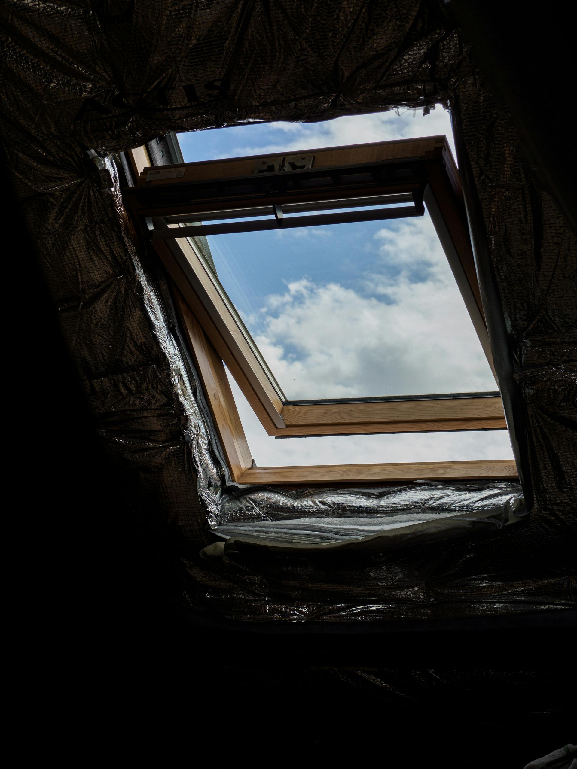 A wooden attic window opens to reveal a clear blue sky and fluffy white clouds.